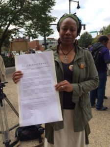Labor Guild board member Khalida Smalls-- District Coordinator for Strategic Partnerships, SEIU 32BJ-District 615-- holds the statement of faith written by clergy standing in solidarity with janitors of SEIU 32BJ